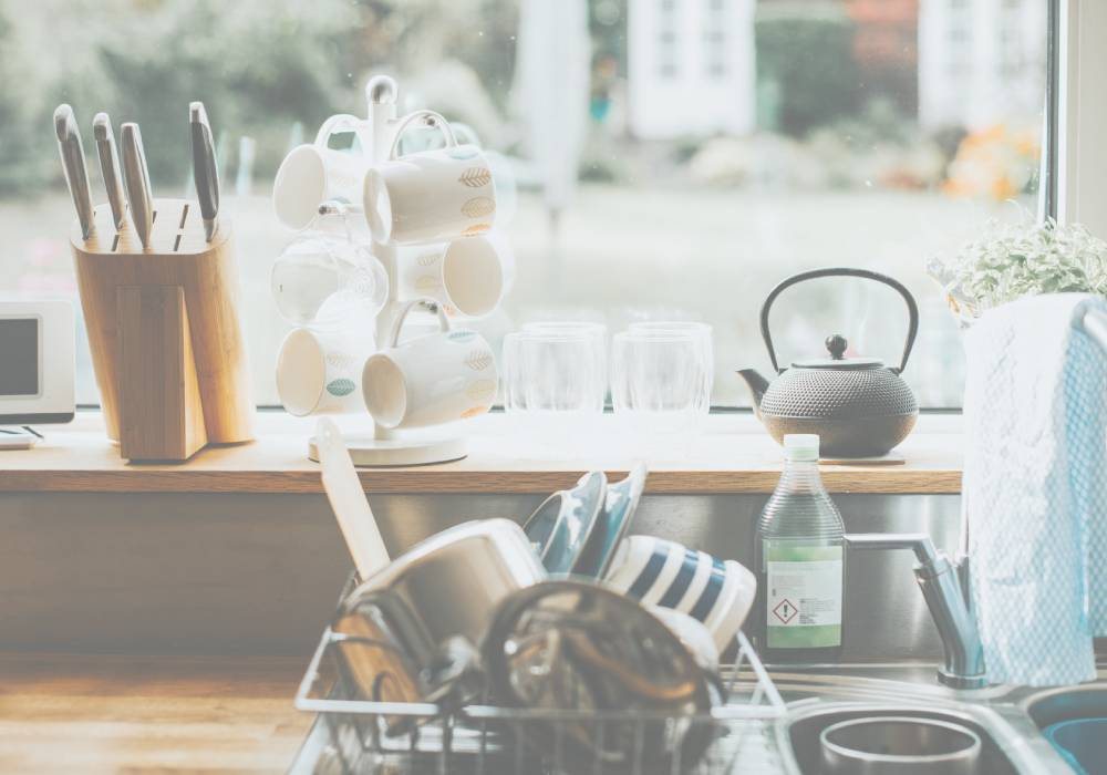 A bright kitchen counter with a kettle, mugs and a dish rack